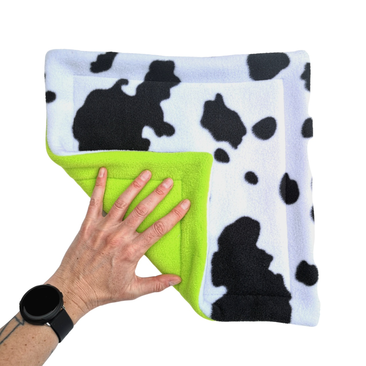 A hand holds a black and white cow print fleece pet pee pad with a like green reverse side