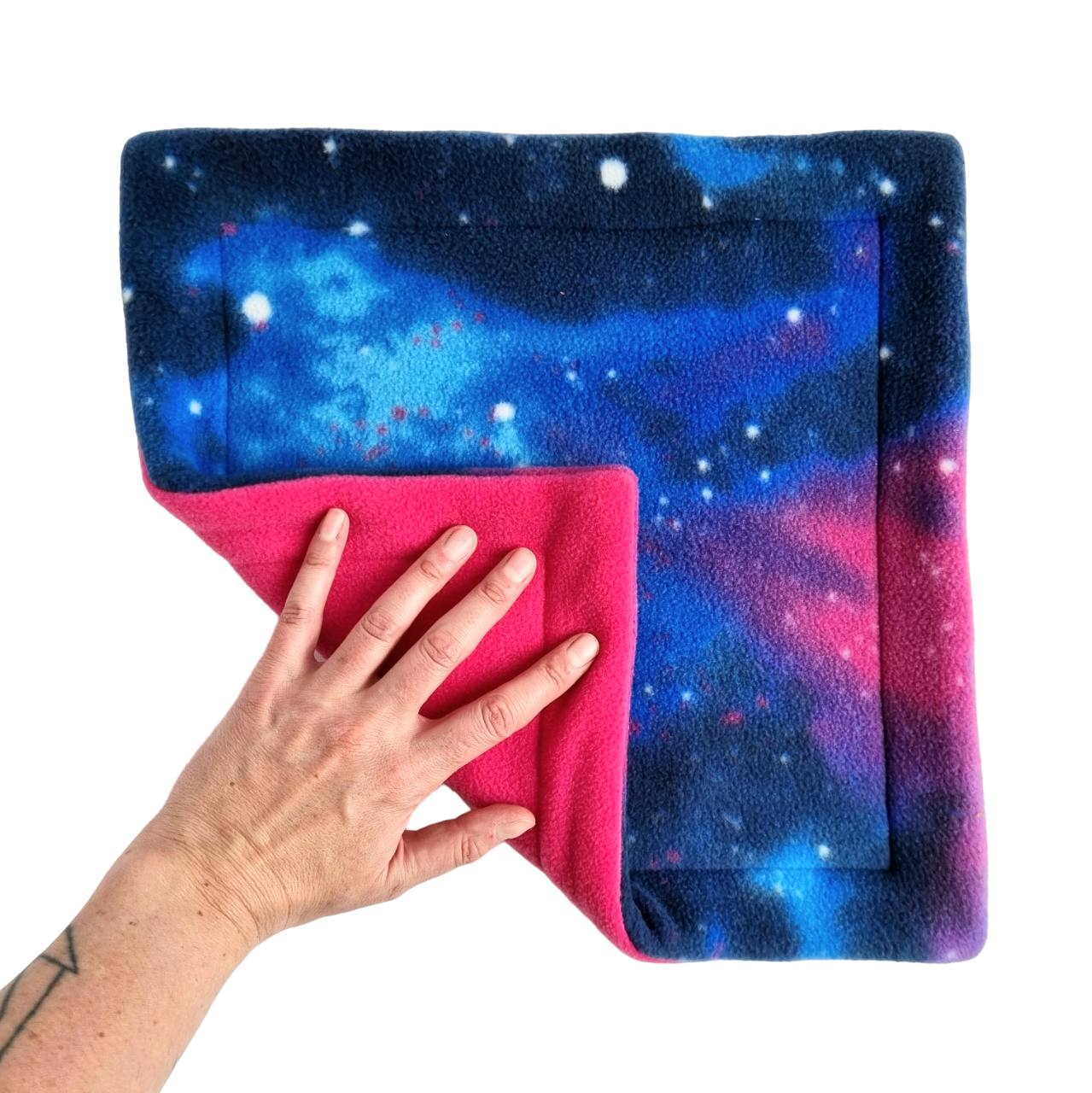 A hand holds a blue and pink galaxy print fleece pet pee pad with a pink reverse side