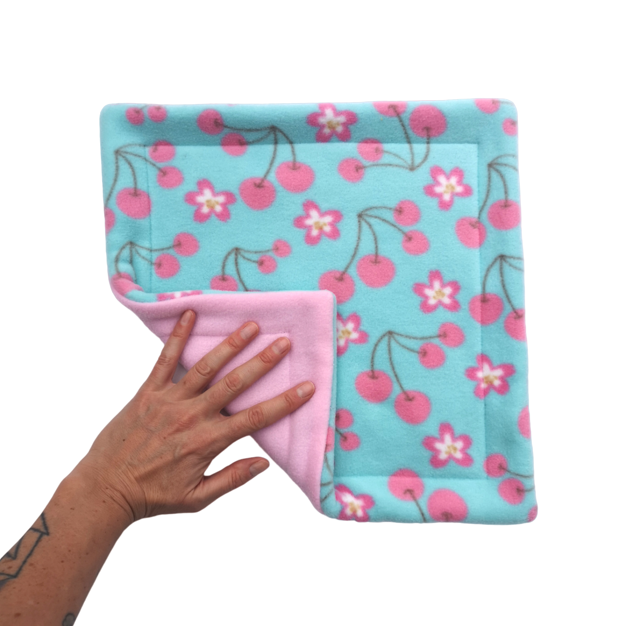 A hand holds an mint green and pink cherry blossom print fleece pet pee pad with a light pink reverse side