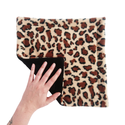 A hand holds a leopard print fleece pet pee pad with a black reverse side.