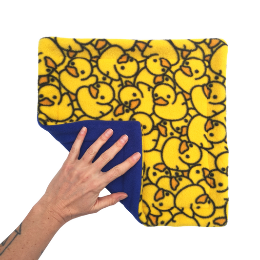 A hand holds a yellow rubber ducks print fleece pet pee pad with a royal blue reverse side